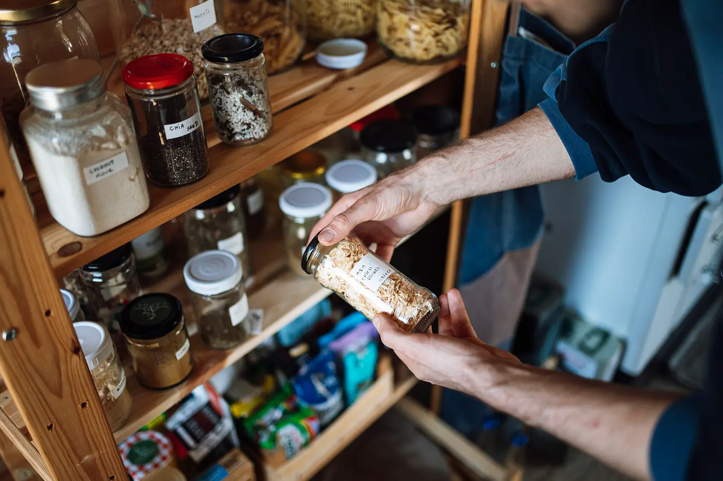 Person picks up a jar from a shelf in a kitchen during the daytime while organizing food items and ingredients