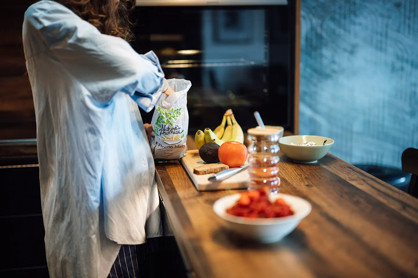 Person preparing food in a kitchen with fruits and ingredients on a wooden table